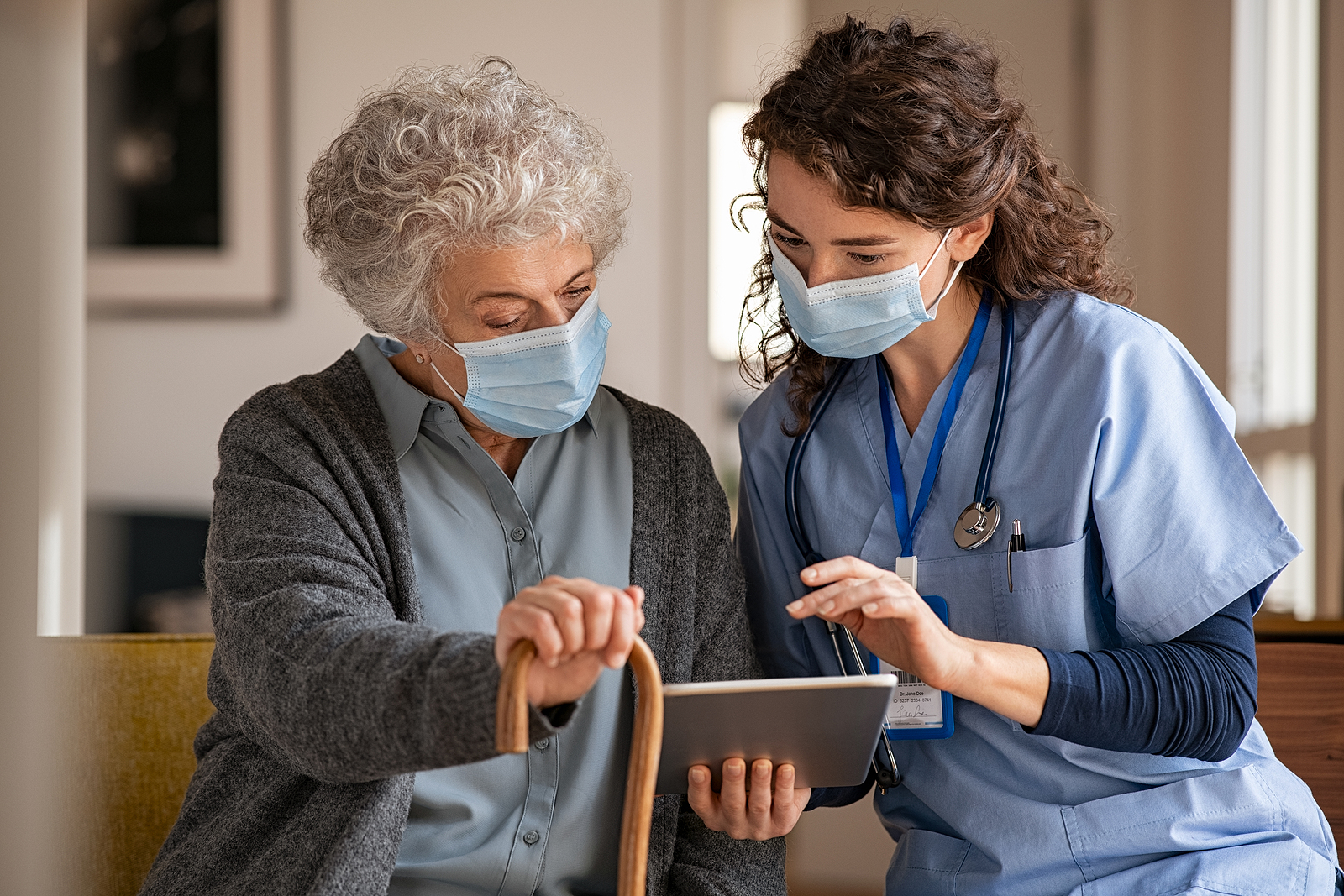 an older vulnerable adult holding a cane, speaking to a doctor. Both women are wearing hygienic masks